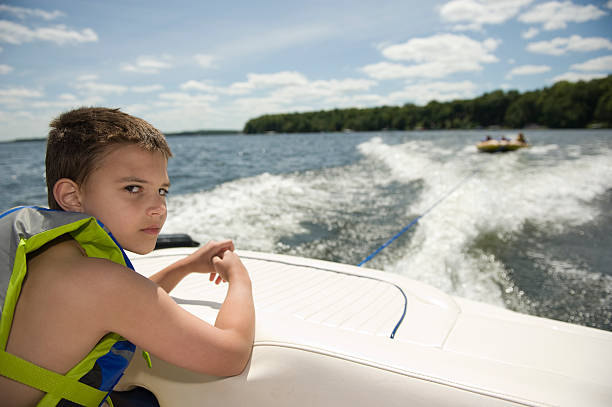 8 ans garçon à cheval sur un bateau - motorboating sailing life jacket lake photos et images de collection