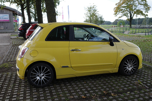 Hardenberg, Netherlands - Oct 2023. A yellow Fiat 500 is parked near the river Vecht
