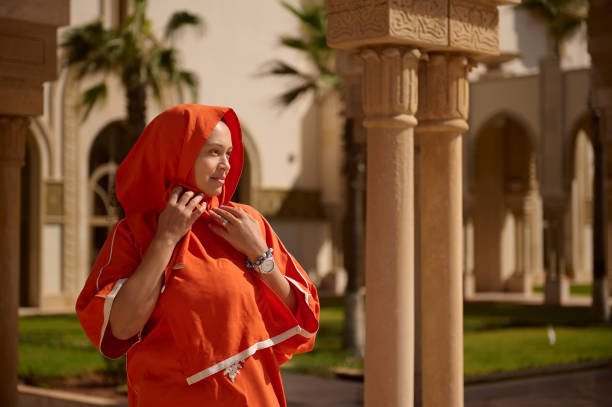 Lovely Muslim woman with head covered in hijab, looking into the distance, standing against Oriental building background