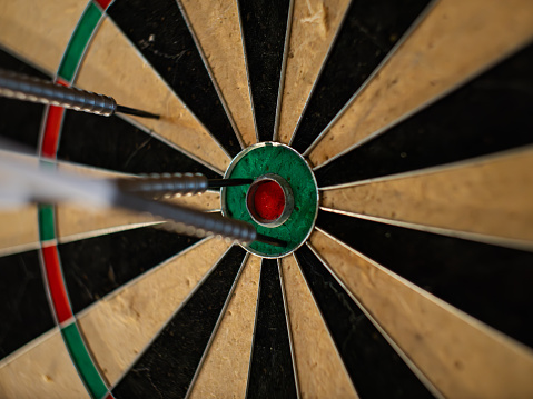 Darts in a dartboard close up. The bullseye is the target but it was missed. The objective is to hit the center. This leisure activity is a popular game in a pub.