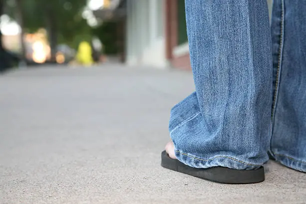 "Closeup of Woman's Sandles, blue jeans, and sidewalk."