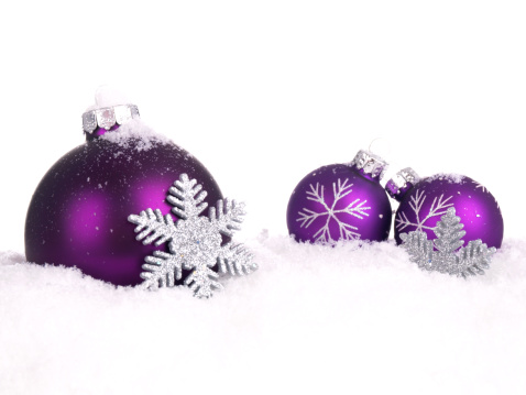 Three purple Christmas balls with silver snowflakes sitting in snow with white background and copy space