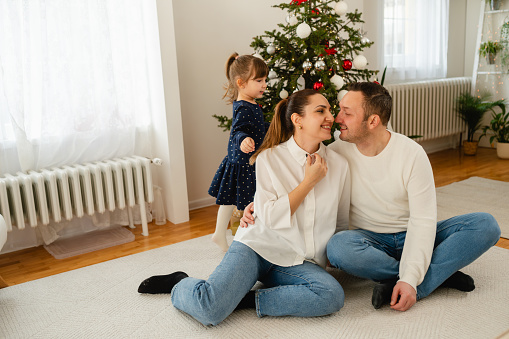 Family sharing love and kisses, bonding in front of Christmas tree and having great time on the holiday season
