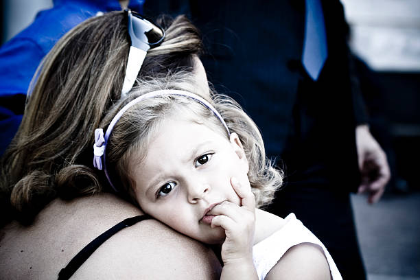 rear view of mother embracing her little girl biting her finger.Nikon D3X / D800. Converted from RAW.
