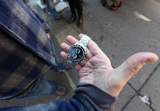 Vendor, with worn fingers, on Canal Street in New York City displaying new plastic wrapped luxury, watch offered for sale.