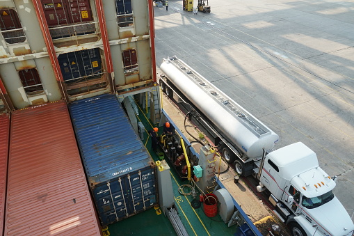 Houston, USA - 06 15 2023: Fuel hose from tanker truck connected by crewmembers to container vessel in bunker station with valves and manifolds during transferring of oil or bunkering.