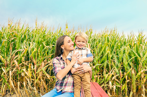 A mother hugging her toddler son outdoors by a corn field.