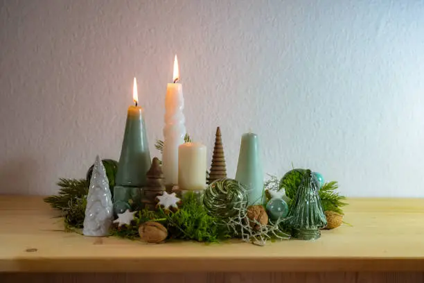 Second Advent, decoration with four different candles, two are lit, green glass Christmas balls, moss and cinnamon stars on a wooden table against a light wall, copy space, selected focus
