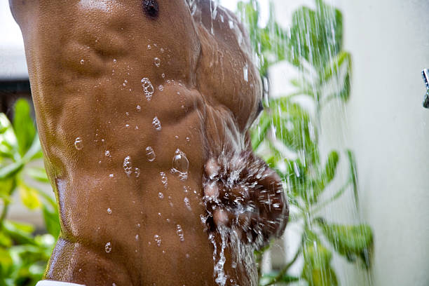 buff male in shower "A buff tanned male is showering. The soap bubbles slide down his wet skin while the motion blur of the falling water hitting his hand gives a dramatic focus to the image. Copy space.  Eos 5d. Squeaky clean health and fitness and spa image. See more below or in my """ shower men falling water soap sud stock pictures, royalty-free photos & images