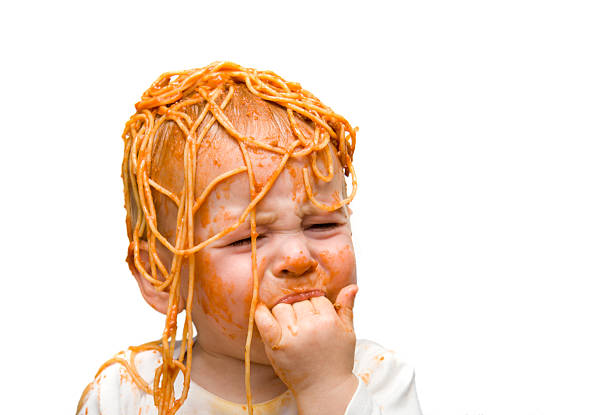 A young baby with spaghetti on their head and face stock photo