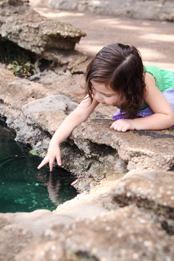 Cute little girl dipping her finger into a pool of water