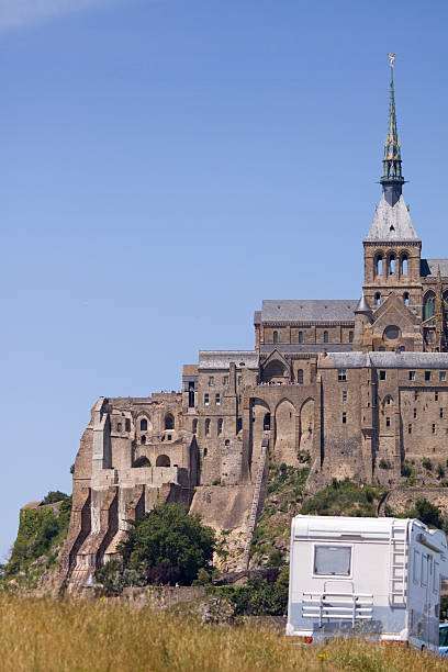 Touring in Normandy "The iconic World Heritage site, Mont Saint Michel, in Brittany France. The rocky tidal outcrop can be seen for miles around, reaching for the sky 1km off the shoreline of the incredibly flat Bay of Mont Saint Michel. It is the number 2 tourist destination in France, behind the Eiffel Tower. The first monastery built on the rock dates from the 8th century, changing through the centuries, with the principal ecclesiastical features being built in the 12th century which was then mostly burnt down in a fire during a siege in 1204. The current architecture with itaas Norman Benedictine Abbey is principally from the rebuild thereafter. The site attracts 3 million visitors a year including many touring, by car or motor home, through this beautiful part of Normandy and Brittany. Good copy space." outcrop stock pictures, royalty-free photos & images