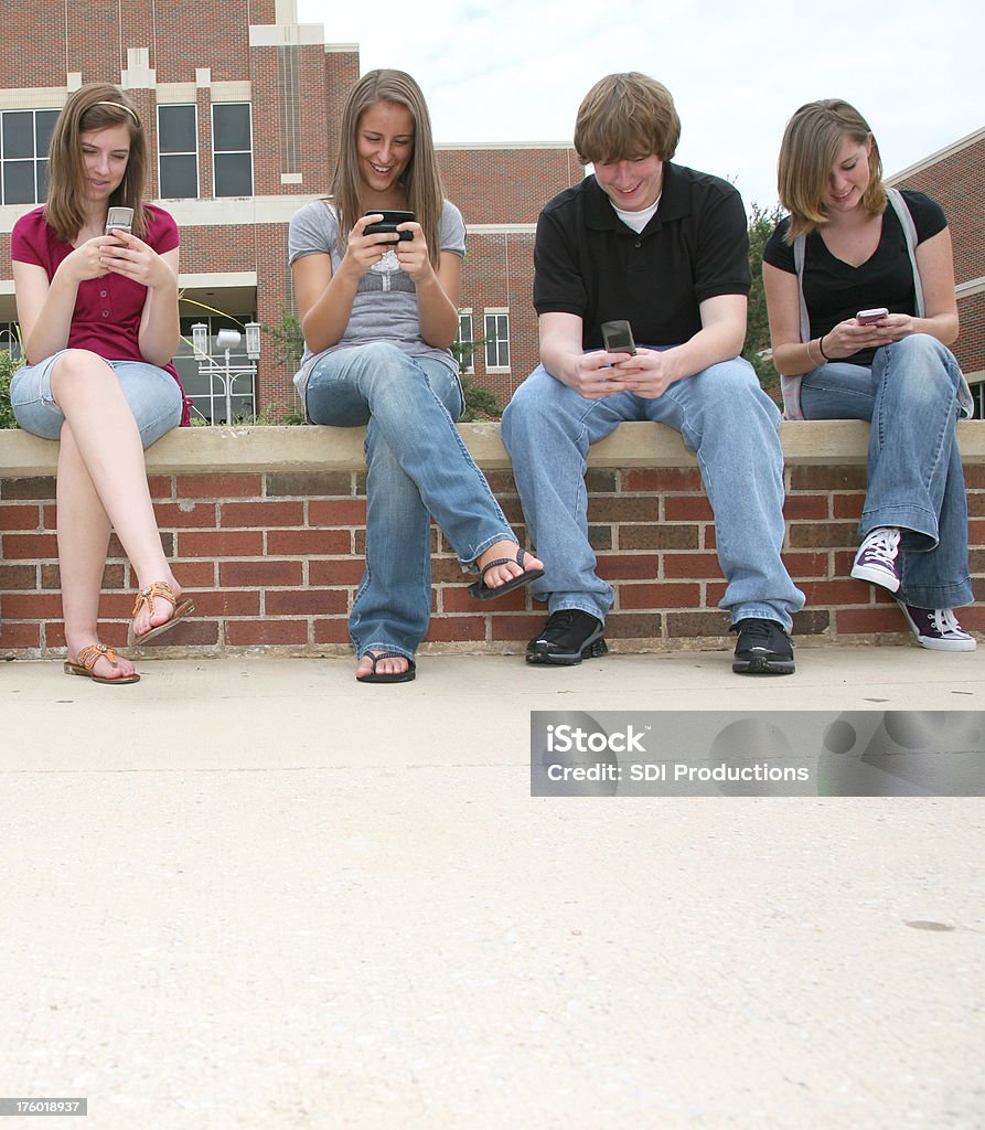 Cuatro High School amigos divirtiéndose SMS en teléfonos móviles - Foto de stock de 16-17 años libre de derechos