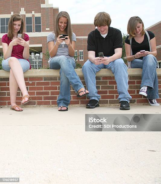 Cuatro High School Amigos Divirtiéndose Sms En Teléfonos Móviles Foto de stock y más banco de imágenes de 16-17 años