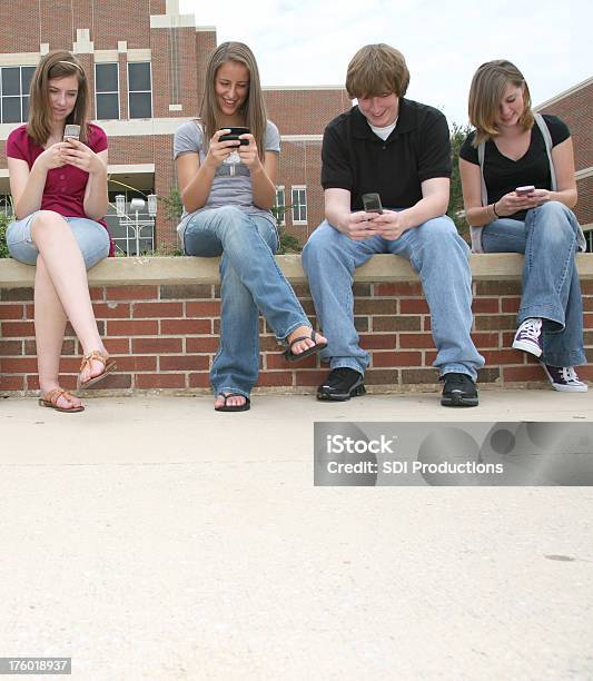 Quattro High School Amici Che Si Diverte Inviare Sms Sui Cellulari - Fotografie stock e altre immagini di 16-17 anni