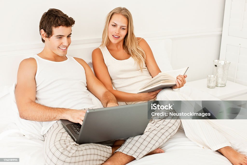 Souriant jeune homme à l'aide d'ordinateur portable tandis que femme tenant livre - Photo de 20-24 ans libre de droits