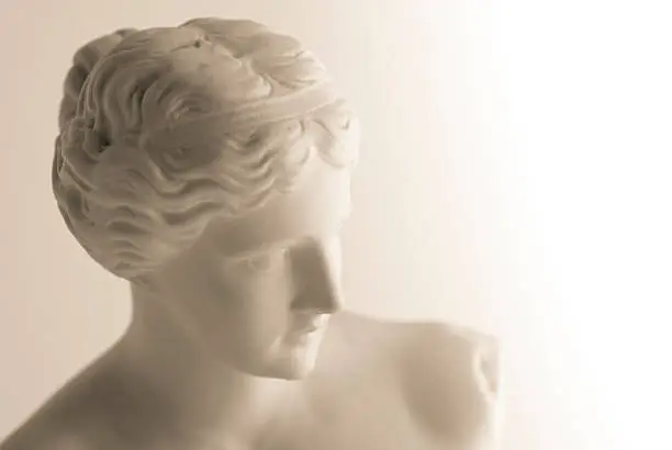 Sepia-toned image of a vintage copy statue of Venus (or Aphrodite) de Milo, a famous Greek sculpture dating back to about 100 BC and found in 1820 on the Aegean island of Milos. The original statue is in the Louvre museum in Paris. The right hand side of the image fades to pure white.