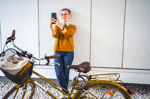 Smiling Caucasian woman with short hair taking selfies in front of a white background beside her bicycle
