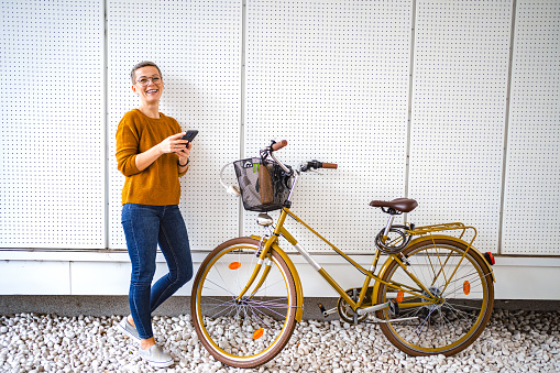 Caucasian woman with short hair using mobile phone while standing beside her bicycle