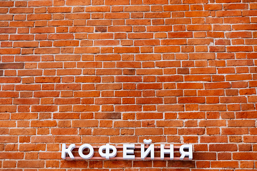 Minimalistic shot of a brick wall with sign. A coffee shop sign on the wall. Announcement on the facade of the building. Red brick masonry. High quality photo