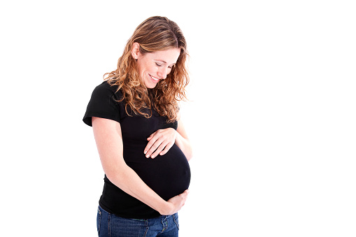 Photograph of a beautiful pregnant woman happily holding her 7 month pregnant belly and looking down; white background with copy space 