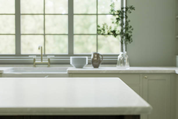 istock Kitchen interior with an island with a white stone countertop - for placing and advertising products against the blurred background of the kitchen by the window. 3D rendering 1760285339