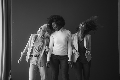 Three multicultural friends dancing and having fun in casual clothing. Group of diverse female friends celebrating and having a good time. Best friends making happy memories. Black and white studio photo