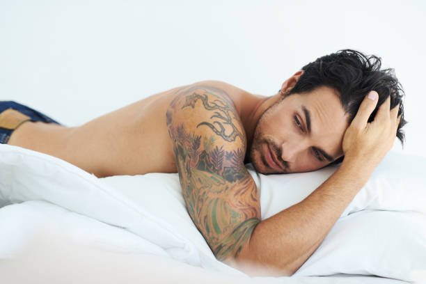 Some mornings are harder than others... Shot of a solemn-looking young man lying face down in his bed chest tattoo men stock pictures, royalty-free photos & images