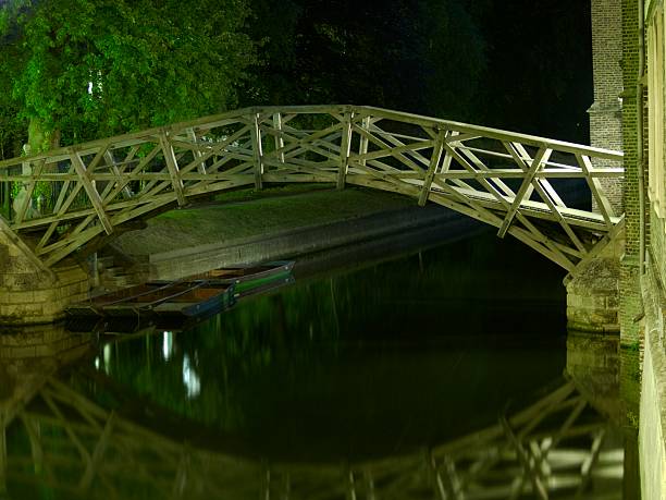Queens' College Mathematical Bridge at night "The so-called Mathematical Bridge over the River Cam at Queens' College, Cambridge University. First built in 1749, it has since been rebuilt to the same design in 1866 and 1905. This is a view from Silver Street. Beneath the bridge are five empty punts - boats used for ferrying tourists up and down the river, usually powered by pole-wielding students." queens college stock pictures, royalty-free photos & images