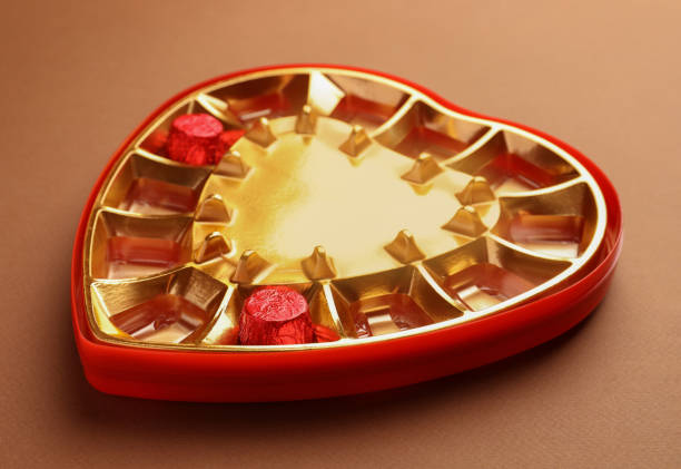Partially empty heart shaped box of chocolate candies on brown background