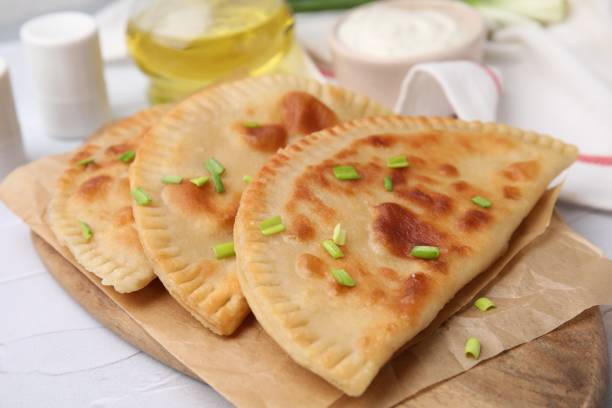 délicieux chebureki frit au fromage et à l’oignon vert sur une table texturée blanche - tatar photos et images de collection