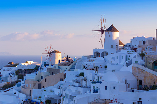 Santorini - Oia, view of white windmills on the slopes of the island. Around are white, picturesque houses between the stone streets. Beautiful sky.