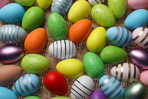 Many painted Easter eggs on burlap, flat lay