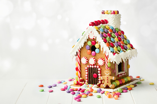 A plate filled with Christmas cookies decorated with frosting and icing for winter holiday celebrations. The baked dessert collection of sweet food features Christmas tree, gingerbread man, snowman, star, heart, and snowflake shapes against the green background of a ceramic plate. The light wooden table area allows for copy space.