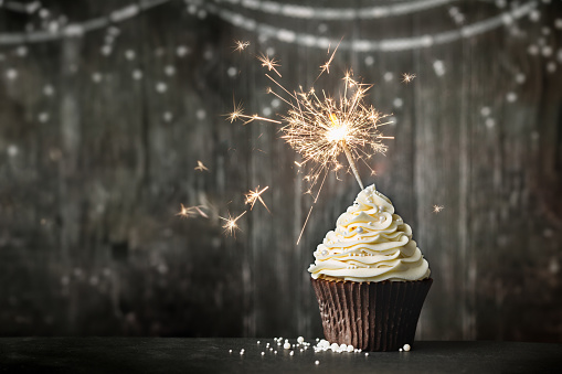 Birthday celebration cupcake with sparkler against a wooden background