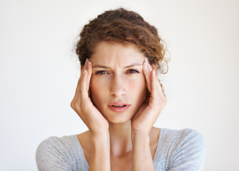 Close up photo of young woman feeling headache, migraine or being ill with short hair in t-shirt touching her head with pain isolated over gray background. Depressed and overworked