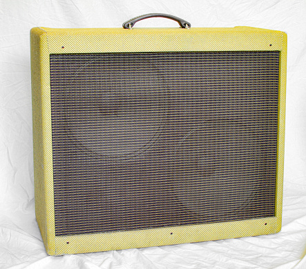 Old vintage retro style fender guitar tube amp or amplifier yellow tweed design with two large speakers visible behind brown grill cover plate.  Isolated on white sheet background Oct 14, 2023 Florida