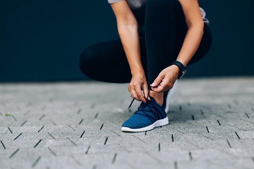 A cropped image of an unrecognizable woman tying her shoelaces before working out outdoors.