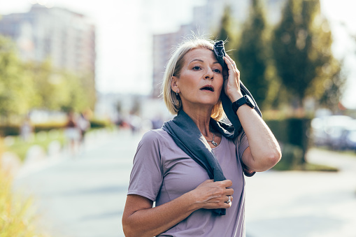 A senior Caucasian woman stopping to catch her breath after jogging in the city.