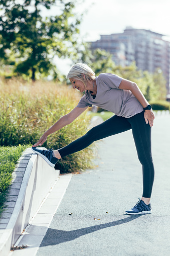 A senior Caucasian woman stretching her legs before working out outdoors.