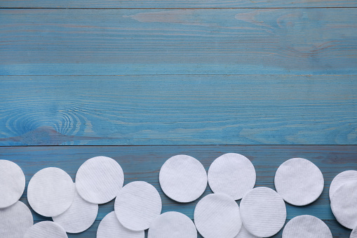 Many clean cotton pads on light blue wooden table, flat lay. Space for text