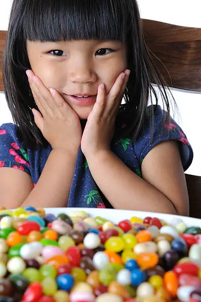 "A young girl puts her hands on her face in surprise, delighted by the giant bowl of colorful jellybeans in front of her."