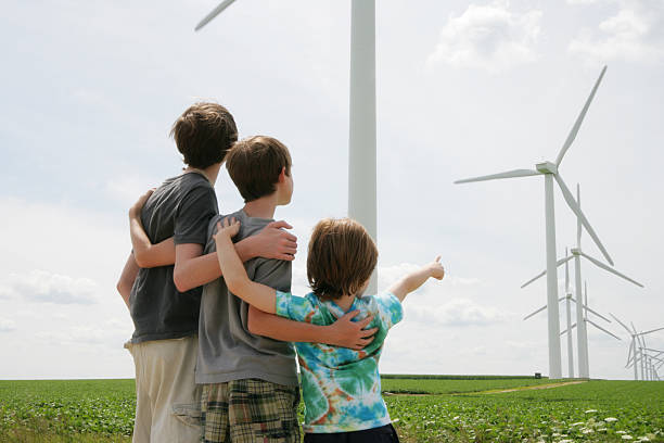 tres niños de pie juntos mirando viento turbines- de energía renovables - parker brothers fotografías e imágenes de stock