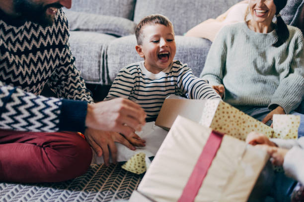 A Cute Baby Boy Opening His Christmas Present While Sitting With His Unrecognizable Parents At Home An excited Caucasian child unwraping his gift while enjoying winter holidays with his family. couple hope sky blue stock pictures, royalty-free photos & images