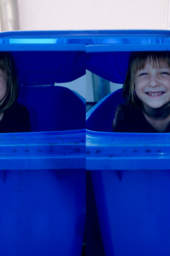 Smiling girl hiding in a blue paper container.