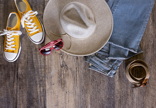 This is an overhead phootgraph of fashion accessories with copy space or a custom product to be dropped into the image. Some of the surrounding border accessories are a brim hat, yellow sneakers, sunglasses, folded jeans and a belt.