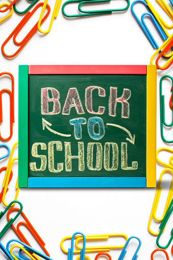 Blackboard with BACK TO SCHOOL lettering hand drawn by colorful chalk.  Lots of colorful paperclips. Isolated on a white background.