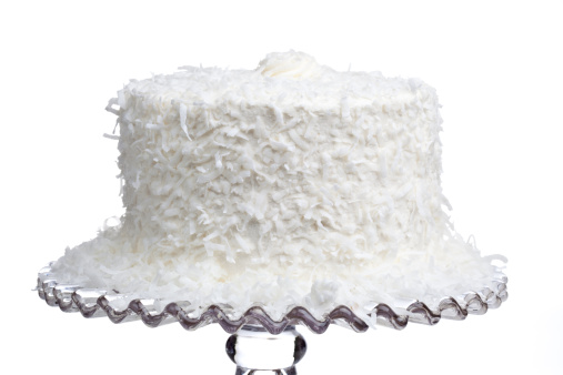 A fresh coconut cake on a glass pedestal on a white background.
