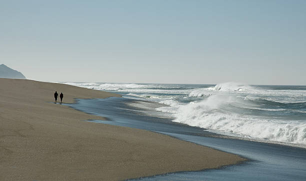 Two figures on unspoiled beach with breaking waves stock photo