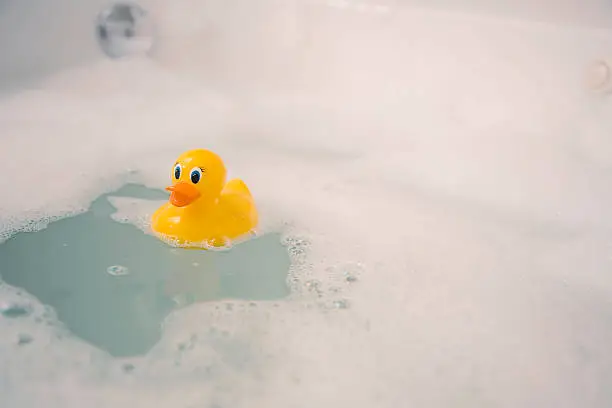 A rubber duckie floats in a bubble bath.